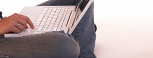 Eine Frau hat ein Laptop auf dem Schoß und Chattet im Internet.